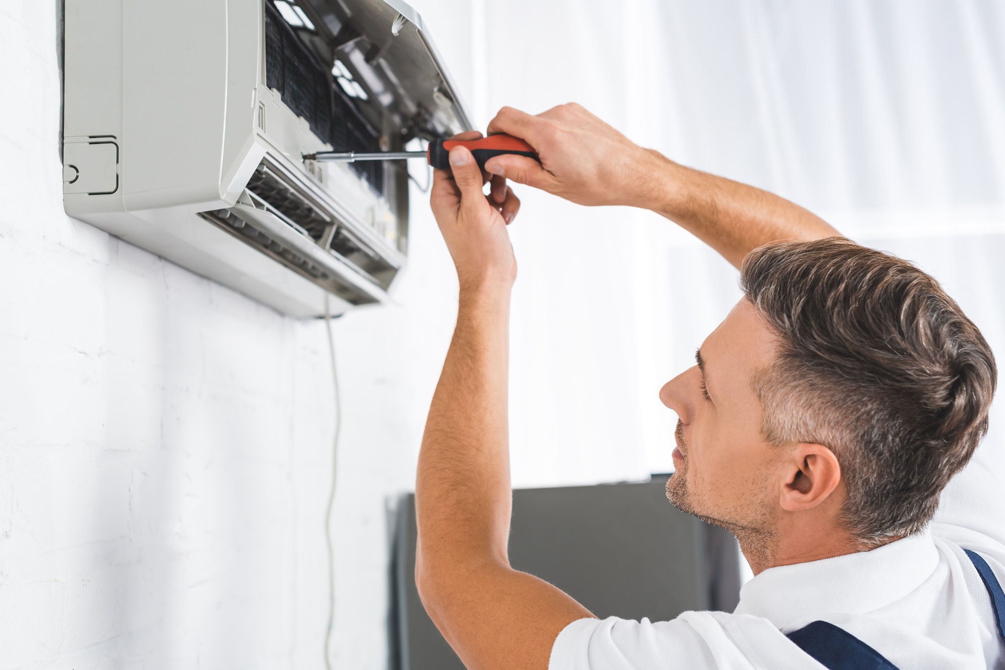 handsome-adult-man-repairing-air-conditioner-with-screwdriver
